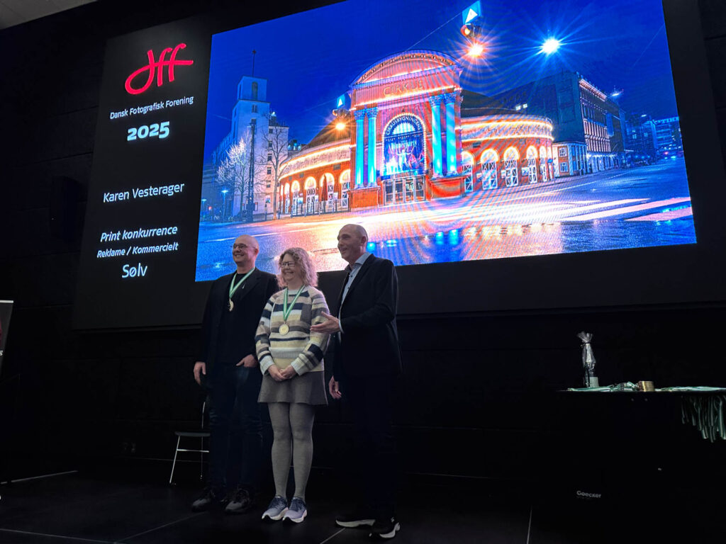 Karen på scenen til dff/Dansk Fotografisk Forenings awardshow i forbindelse med Årets Fotograf 2025. Hun får en sølvmedalje for billedet "Showtime" af Cirkusbygningen i Køebnahvn. Hun står på scenen sammen med Morten Rygaard, der  også fik medalje og formand for dff Kim Poulsen.