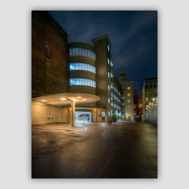 Kunstværket “Backyard Parking” er original fotokunst fra København, der leveres signeret og nummereret i Limited Edition. I en baggård i Dronningens Tværgade ligger der et parkeringshus, som oser en forsvunden tid. Det er lidt af en arkitektonisk og tidstypisk perle i vores optik. I baggrunden kan man lige ane toppen af Marmorkirken.