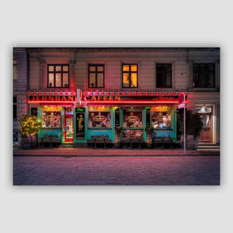 “Jernbanecafeen” er dansk fotokunst, der leveres signeret og nummereret i Limited Edition. Jernbanecefeen ligger bag Københavns Hovedbanegård og er et rigtig værtshus med øl og hygge og alskens ting og sager relateret til tog og jernbaner. Den flotte farverige facade med det røde neonskilt får det til at se hyggeligt ud.