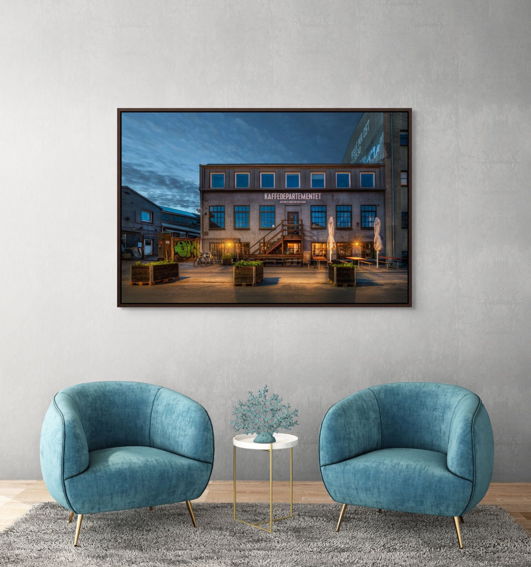 Mockup af kunstværket "Kaffedepartementet" af Surland & Vesterager. Billedet hænger i noget der kunne være et receptionsområde i en virksomhed eller hotellobby på en lysegrå væg bage to turkise stole.
